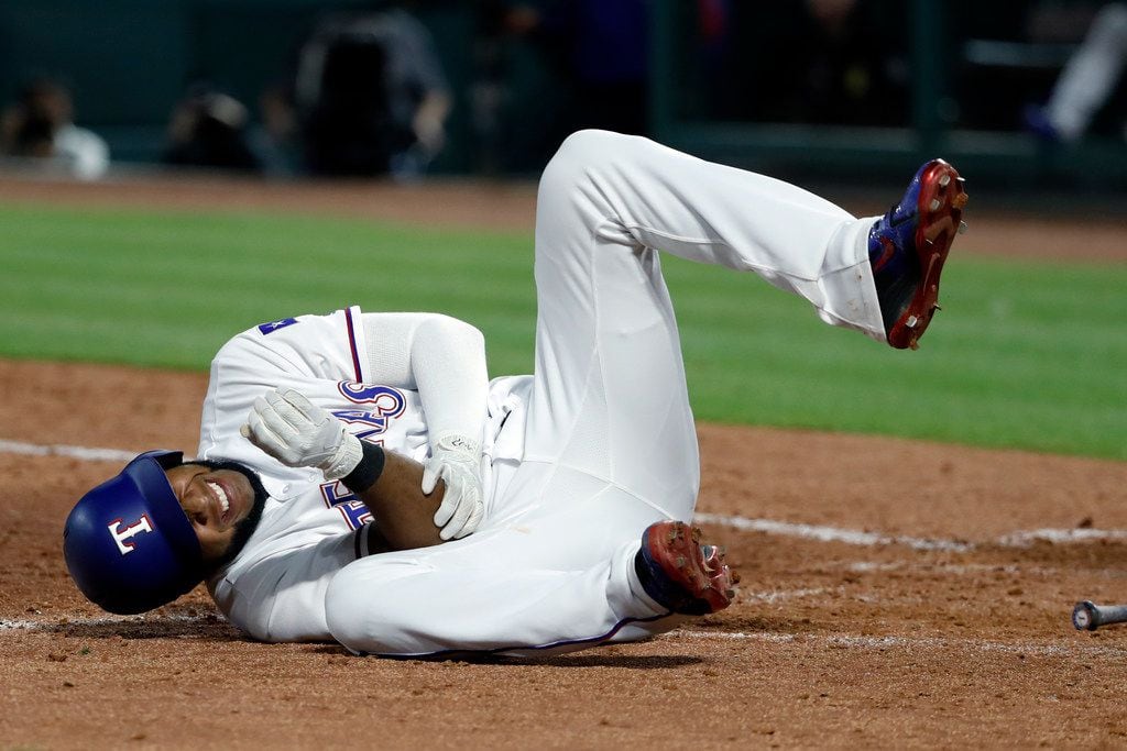 Texas Rangers' Elvis Andrus rolls on the ground by home plate holding his right elbow after...