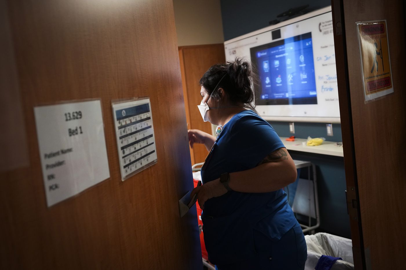 Nurse resident Jaime Luna peeks through a doorway into a patient room in the COVID-19 unit.