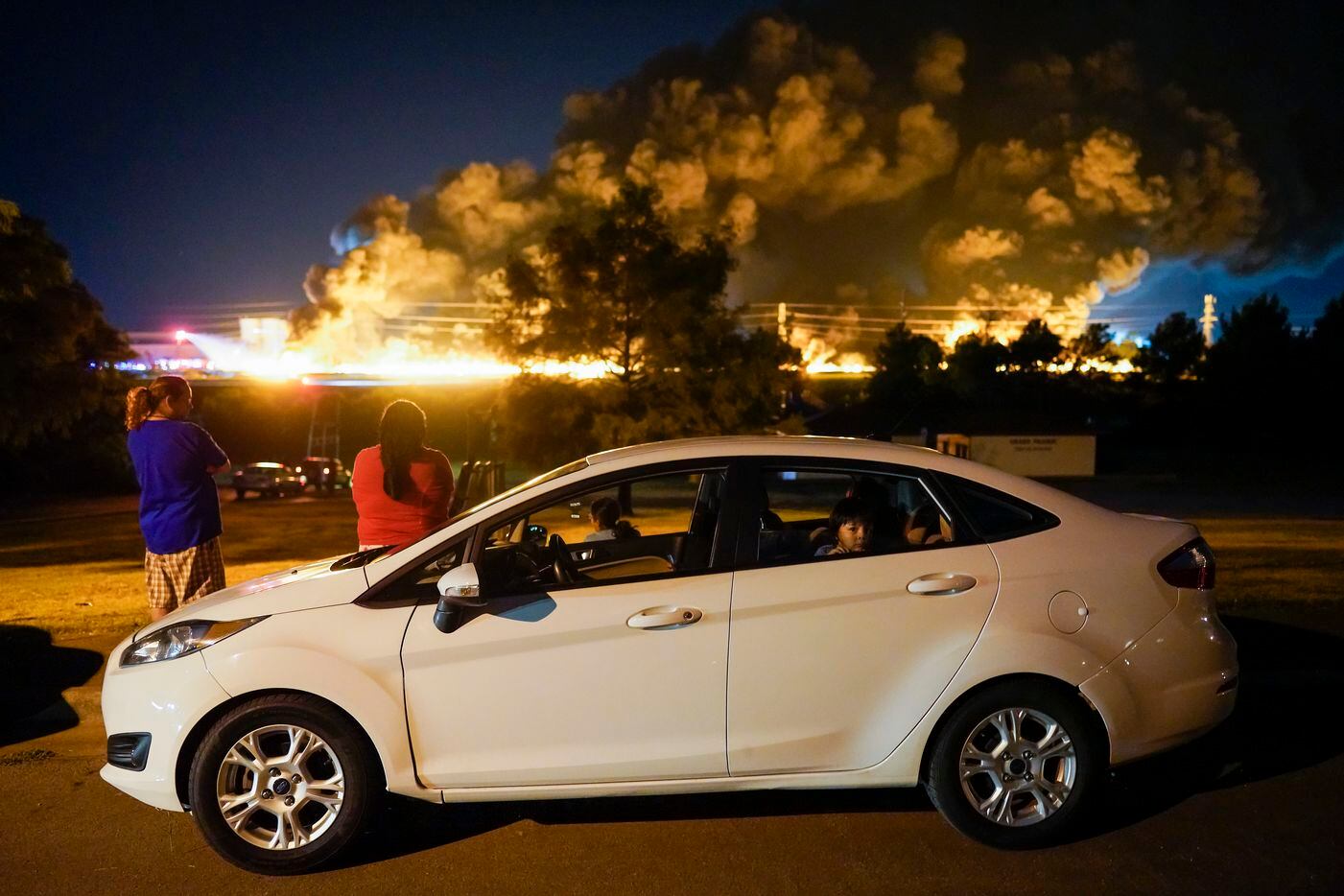 People watch from Tyre Park as fire crews battle a massive blaze in an industrial area of Grand Prairie, Texas, in the early morning hours of Wednesday, Aug. 19, 2020. The fire is in the 2000 block of West Marshall Drive, near the Bush Turnpike. Among the businesses in the area is Poly-America, a company that produces trash bags and other plastic products. (Smiley N. Pool/The Dallas Morning News)