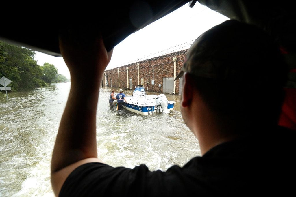 Volunteers in a boat wade through flood waters behind a strip shopping center in Dickinson,...