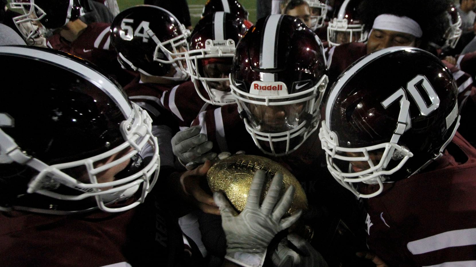 Members of the Red Oak Hawks marvel at the golden football atop a trophy presented after...