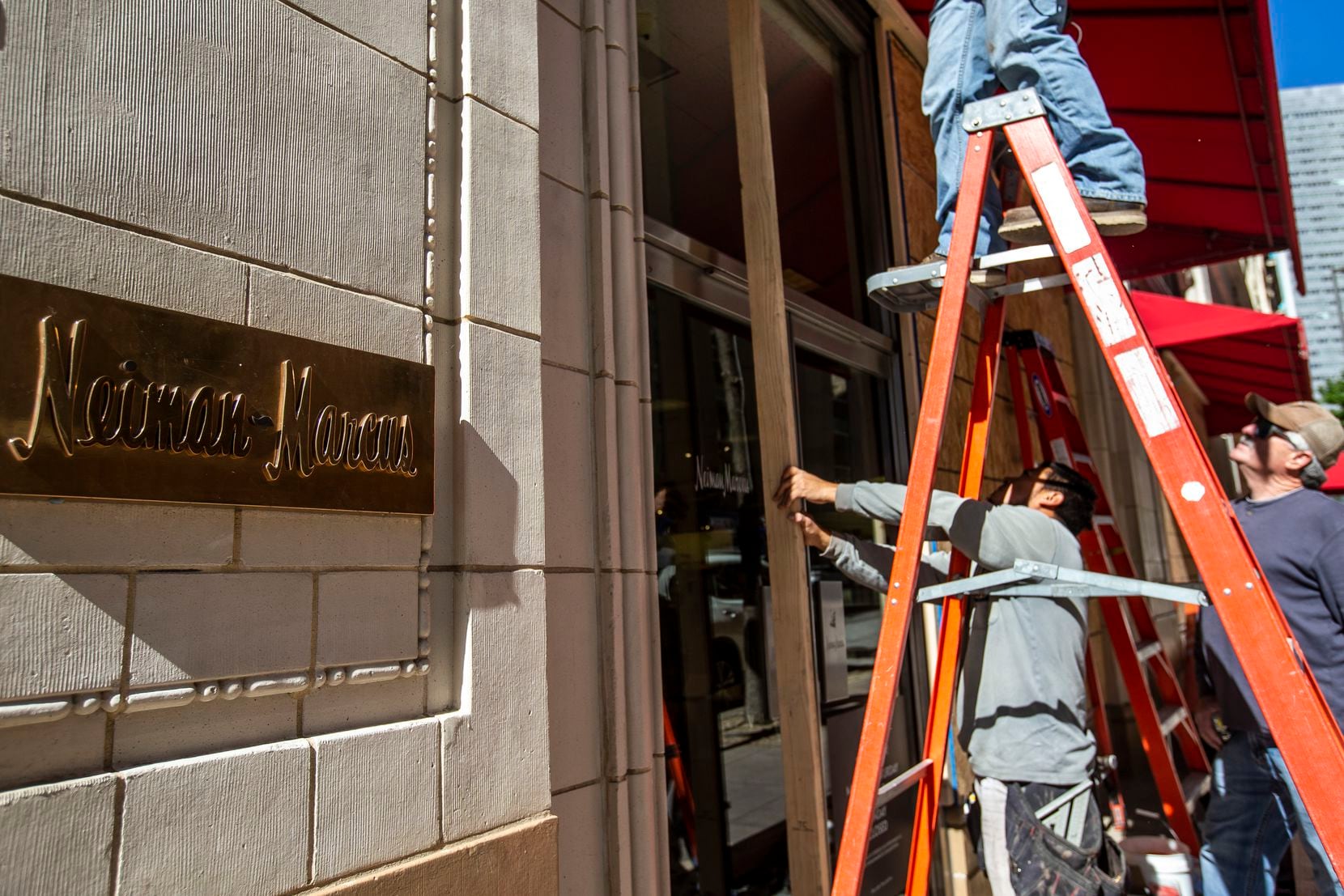 Manuel Tiscareño (center) and Harold Welch, employees at County Glass LLC, board up the storefront at Neiman Marcus in downtown Dallas on Monday, Nov. 2, 2020. Businesses throughout Deep Ellum and downtown Dallas hired various contractors to board up their buildings to deter against possible looting that might occur after the general election. (Lynda M. González/The Dallas Morning News)