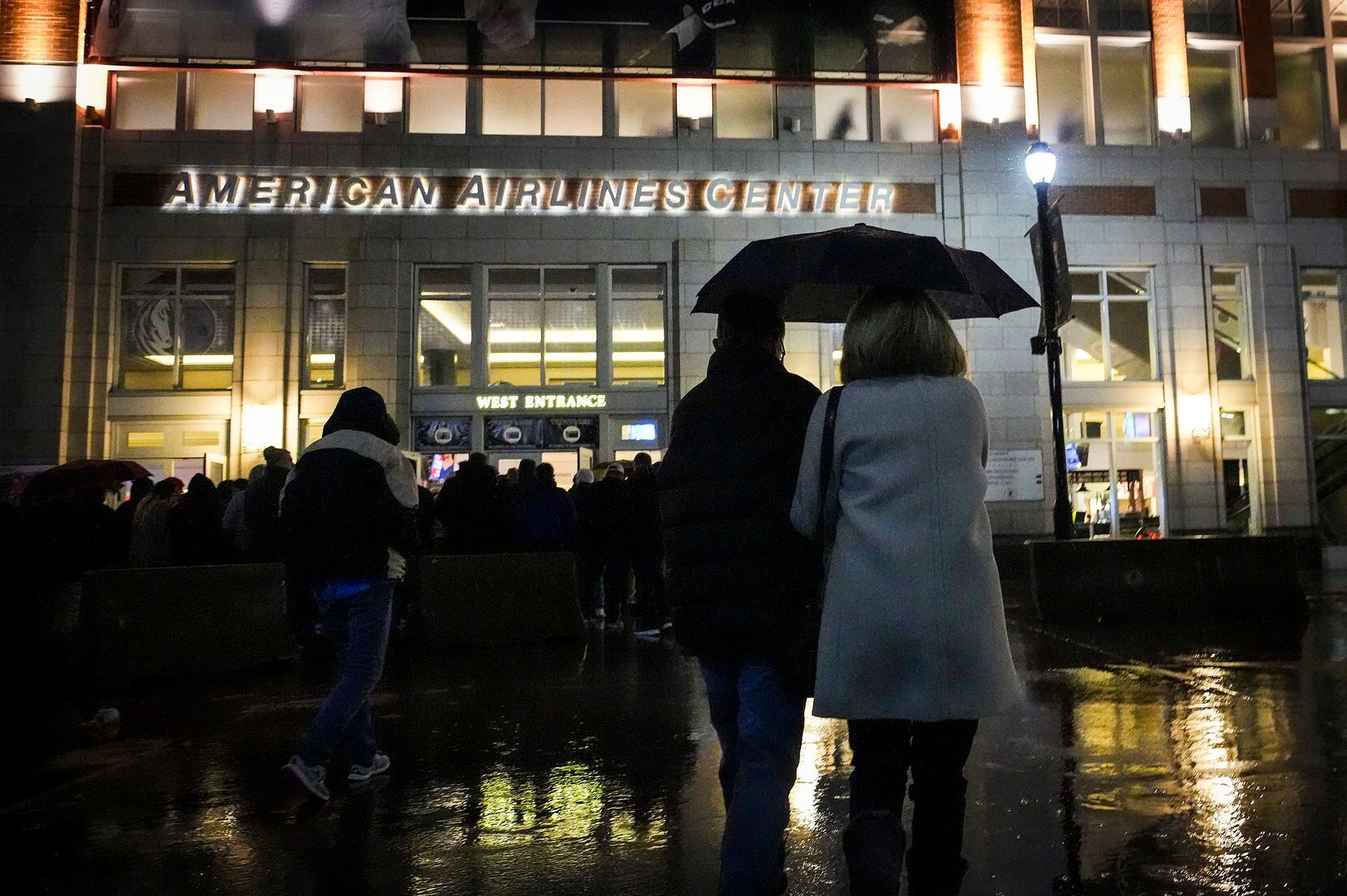 Fans take cover from a cold rain as they head to the American Airlines Center before a game...