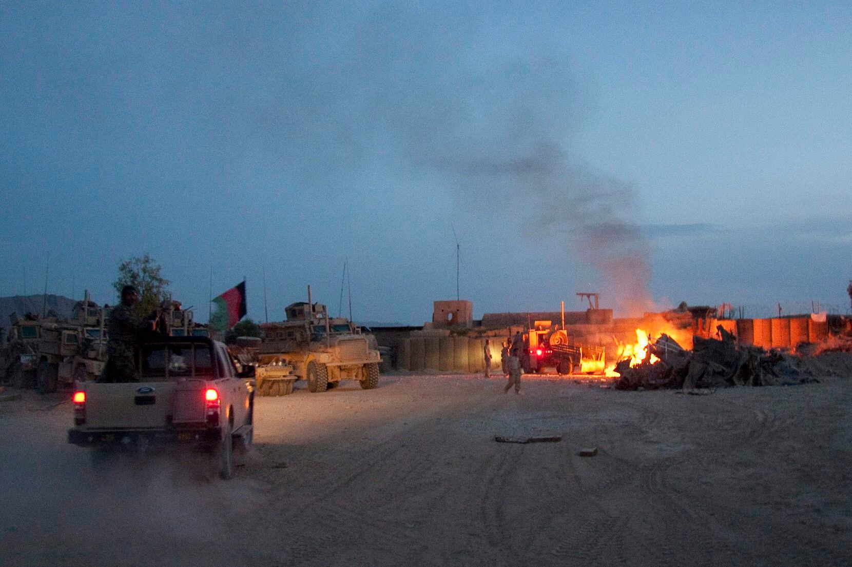 An Afghan National Army pickup truck passed parked U.S. armored military vehicles, as smoke...