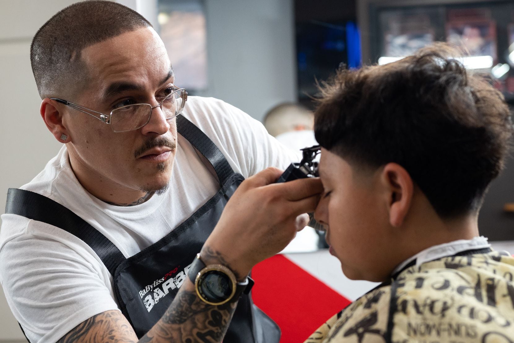 Hairdresser Edgar "E" Montelongo, 35, uses a trimmer to cut the hair of Nathan Cabrera, 12, as he…
