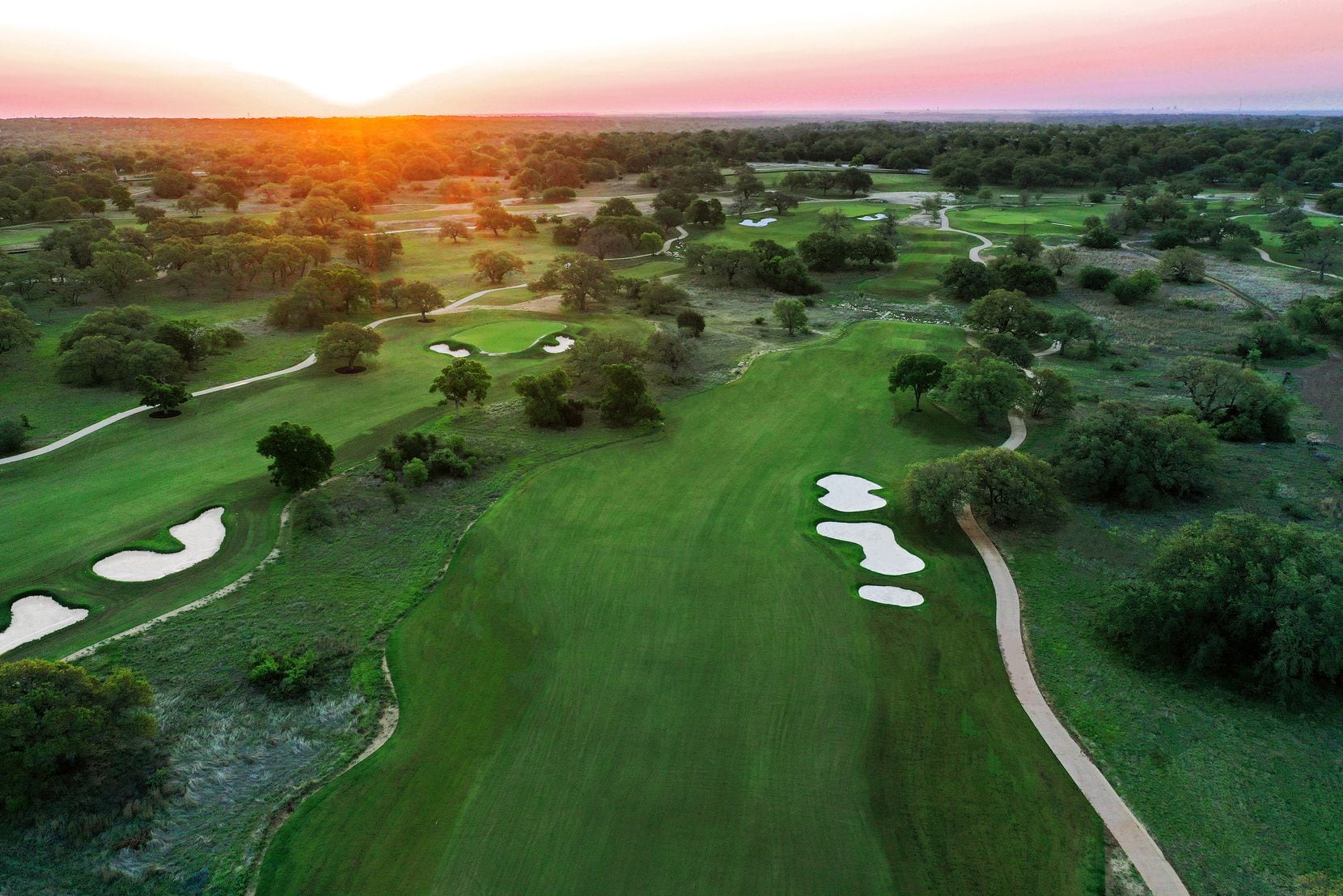 As the sun rises over Driftwood Golf and Ranch Club, several holes on the grassed-in front nine are visible. The holes primarily pictured are Holes 4 & 5 fairway (5 fairway and green on the left, No. 4 fairway and tees on the right). Holes 3 & 6 can be seen at the top of the image.