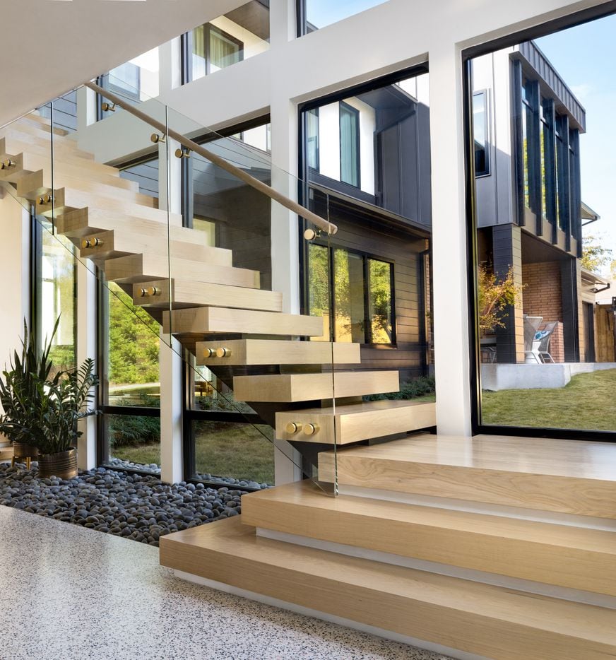 This custom-designed Lakewood home has a floating staircase set beside large glass windows....