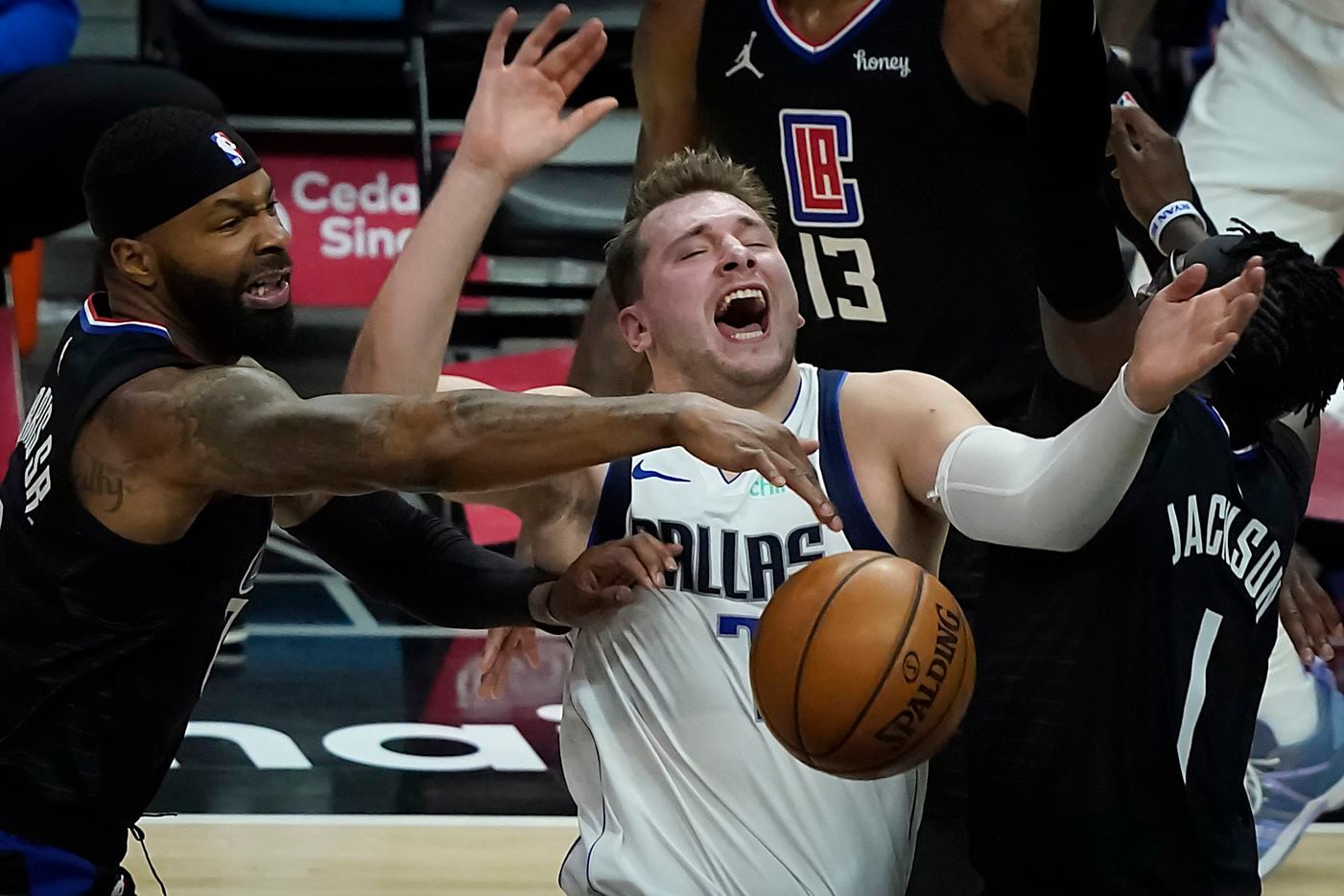 Dallas Mavericks guard Luka Doncic (77) is fouled as he tries to drive between LA Clippers forward Marcus Morris Sr. (8) and guard Reggie Jackson (1) during the first half of an NBA playoff basketball game at Staples Center on Tuesday, May 25, 2021, in Los Angeles.