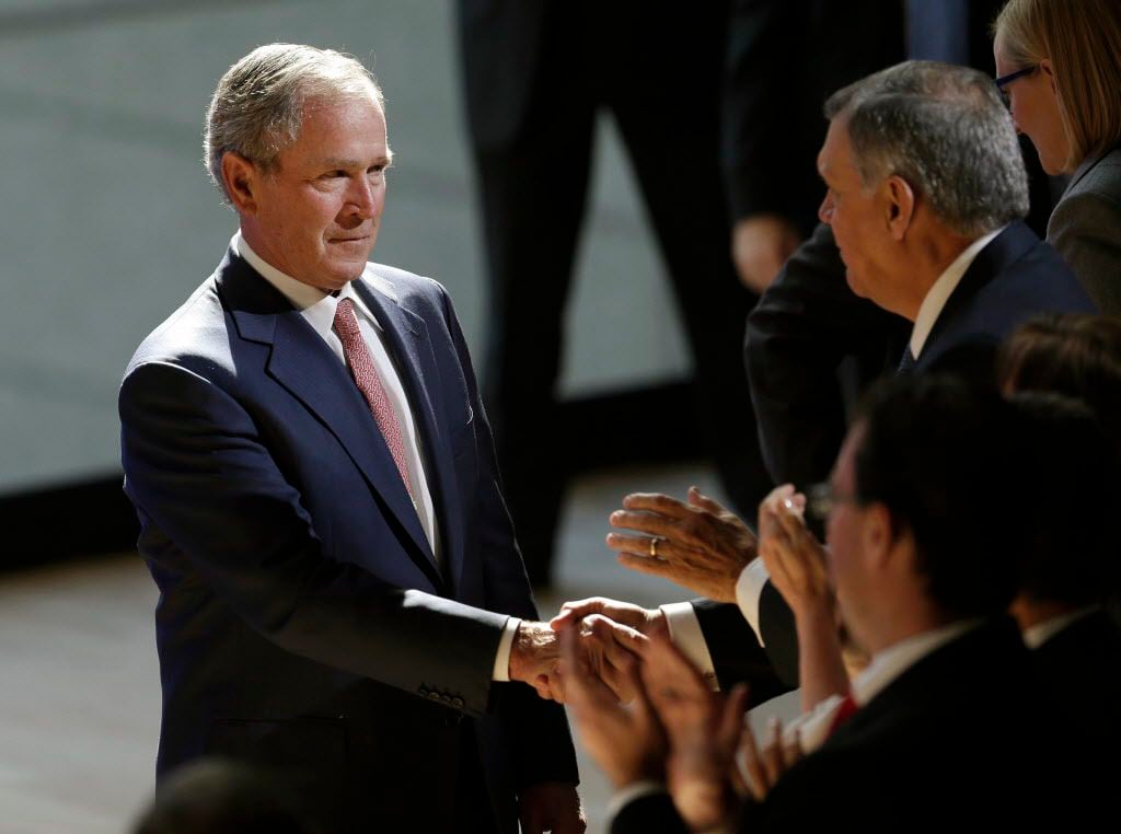 Former U.S. President George W. Bush shakes hands with audience members after speaking at a...