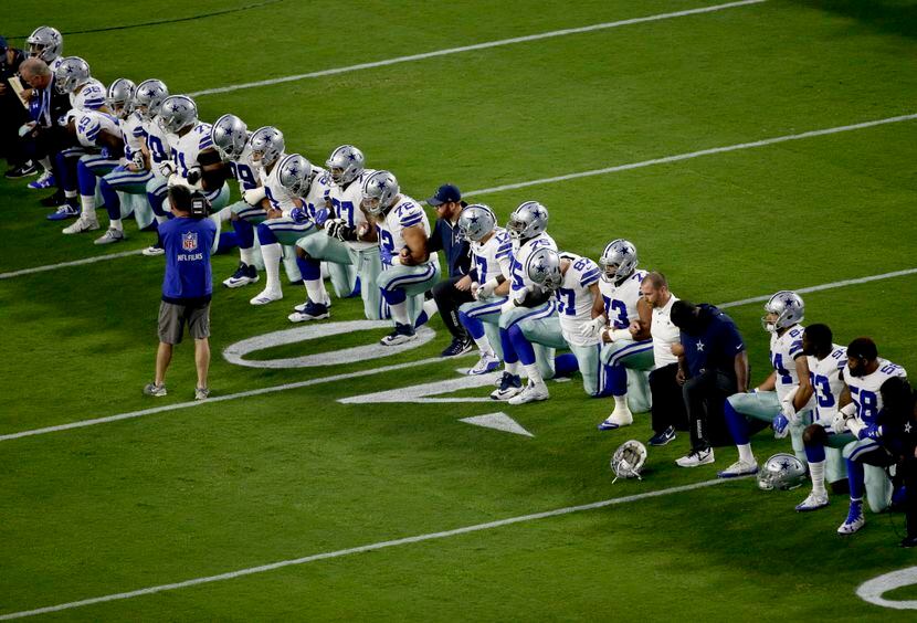 Jugadores, entrenadores y directivos de los Cowboys de Dallas se hincan en el campo, justo...