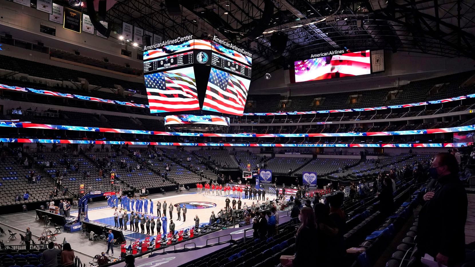 The Dallas Mavericks and Atlanta Hawks, along with a limited fan attendance, stand during...