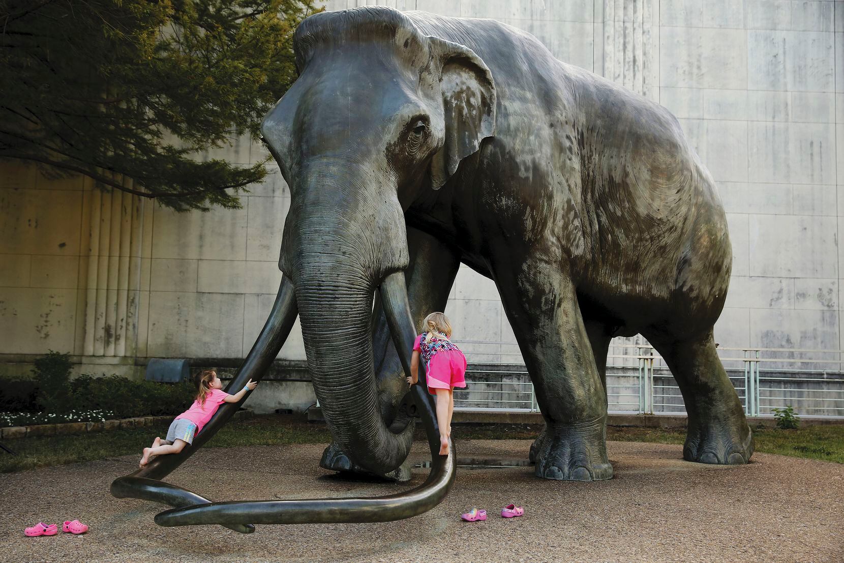 Erin (left), 3, and her sister Ella, 5, of Waxahachie climb on an elephant statue outside the Dallas Museum of Natural History at Fair Park in Dallas.