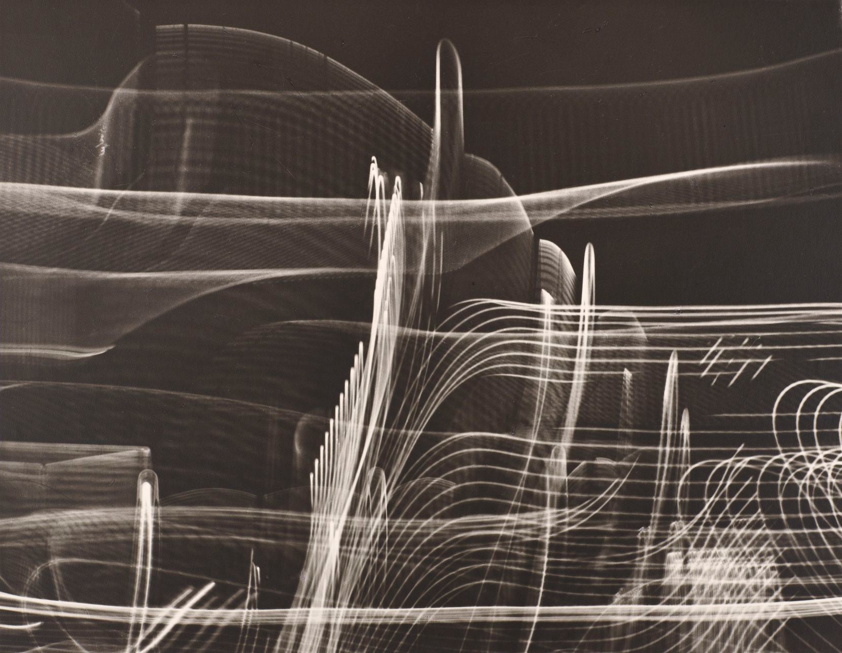Carlotta Corpron was associated with the Bauhaus movement and played a significant role in establishing photography in North Texas. The exhibition features her image “A Walk in Fair Park, Dallas,” one of her highly experimental “light drawings,” black-and-white abstractions she made by moving her camera around while the shutter was open. 