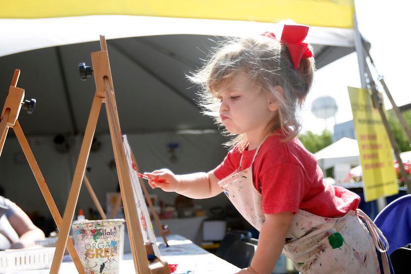 Aria Orana, 2, paints a canvas at the children’s “creation station” area during the annual...