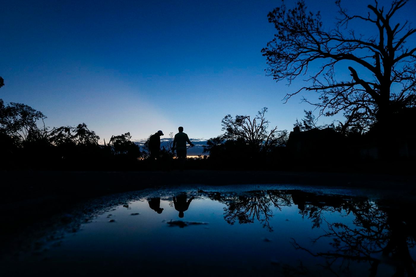 As the sunrises, homeowners Dennis Gambow, left, and Eric Charton emerge to survey damage...