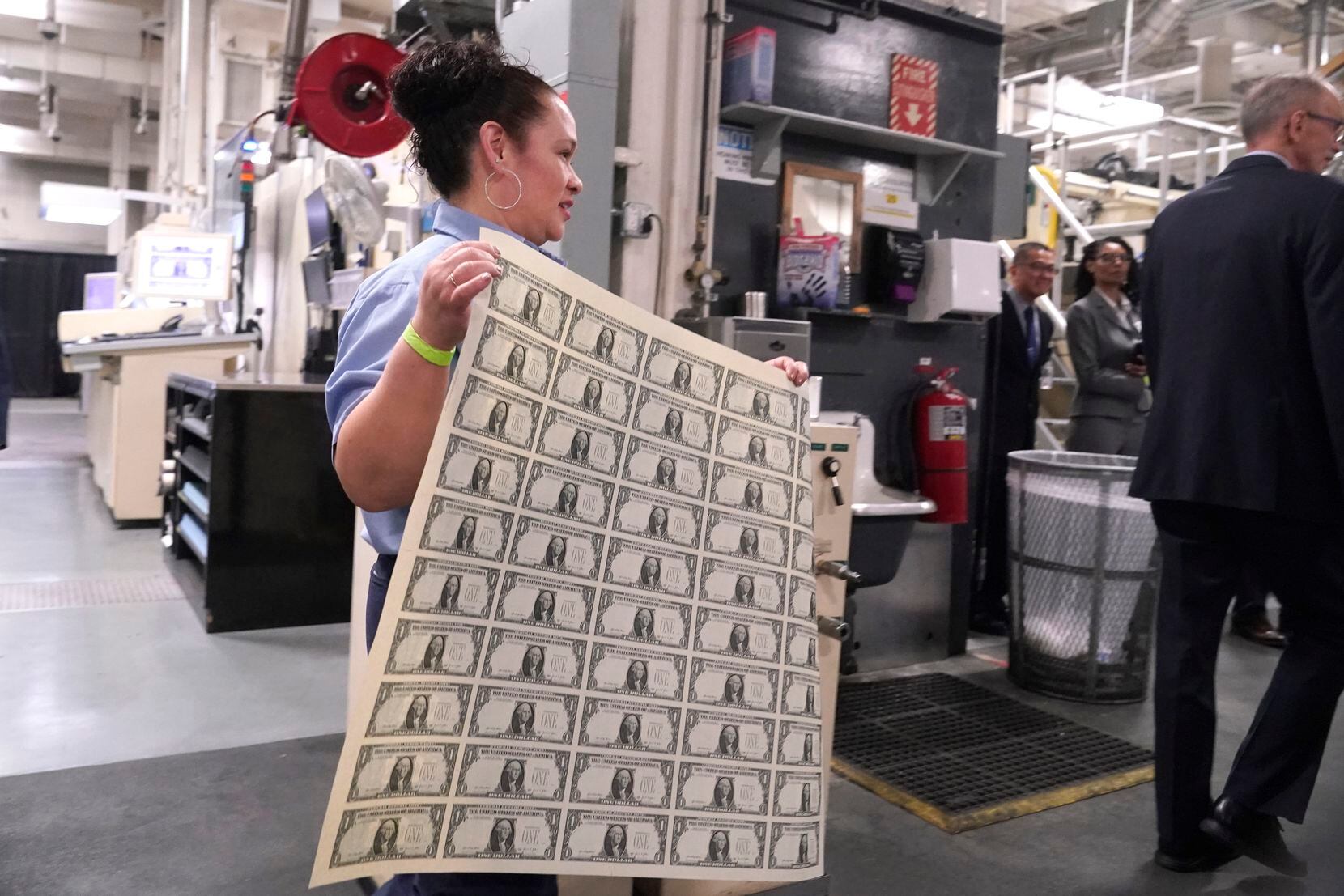 A worker carries a sheet of newly printed $1 bills bearing Janet Yellen's signature.