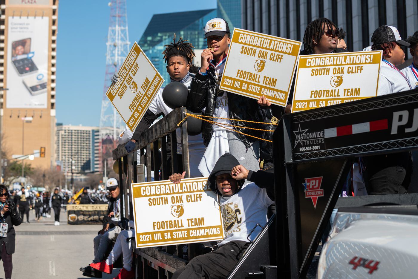 Members of the South Oak Cliff High School football team, ride on a trailer with signs and...