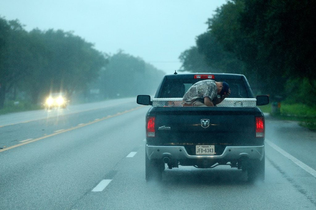 A man shield his face from the wind and rain as he gets a ride in the bed of a pickup in...