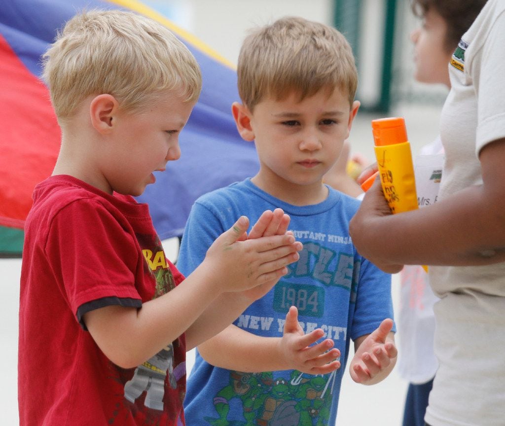 Flynn Willis (left) and Teak Noles apply sunscreen as they play outside at Children's...