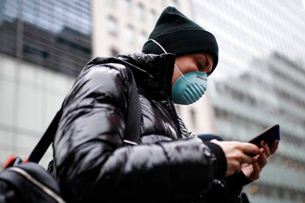 Una persona usa su teléfono celular, y también su máscara, para protegerse del coronavirus...