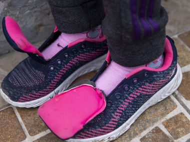 The shoelaces are missing from the shoes of Maria Francela Julag, 8, as she waits with her...