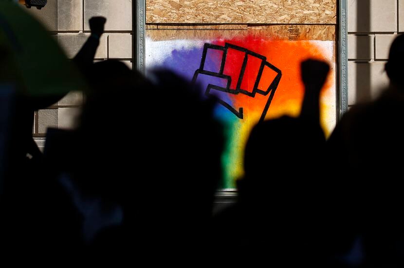 Protesters raise a fist as they pass by a boarded up window on St. Paul Street in downtown...