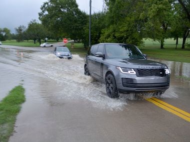 A Range Rover and a car drive through waters flooding out of the banks of White Rock Creek...