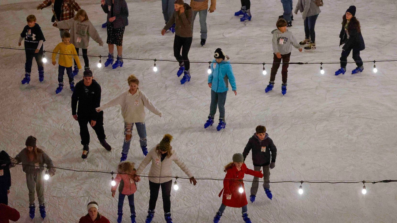 Ice skaters glide underneath strings of lights at the Peace Plaza Ice Rink in front of...