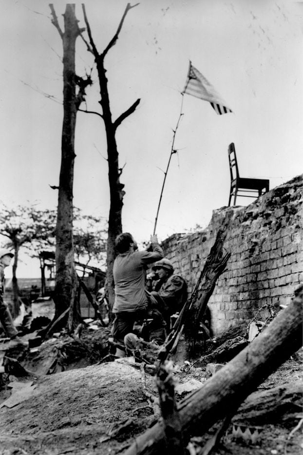 A U.S. Marine waves an American flag tied to a tree branch before securing it on the brick...