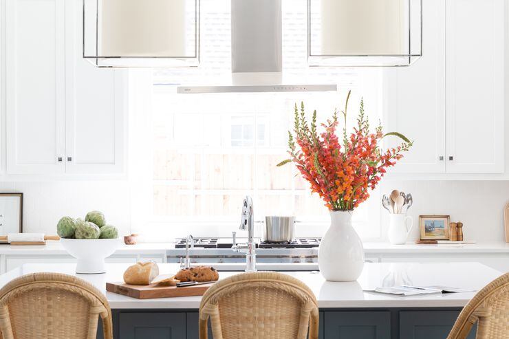 A thin, modern vent hood allows natural light to flow into a white kitchen with orange...