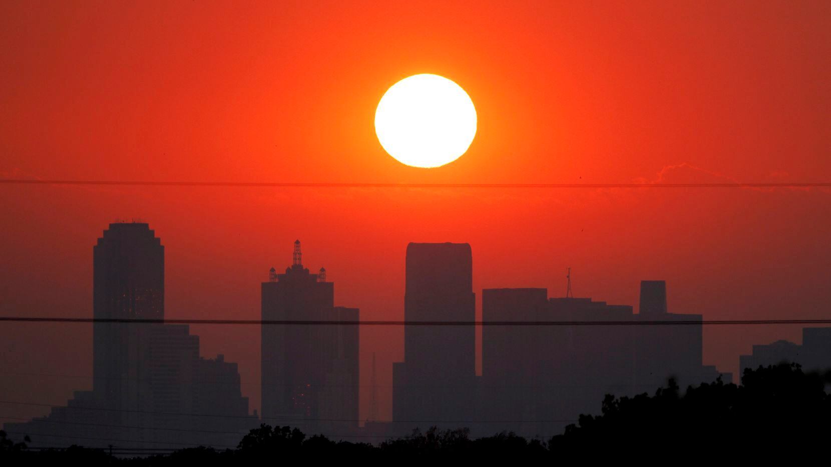 The sun sets beyond a humid city skyline following the storm that passed through Dallas,...