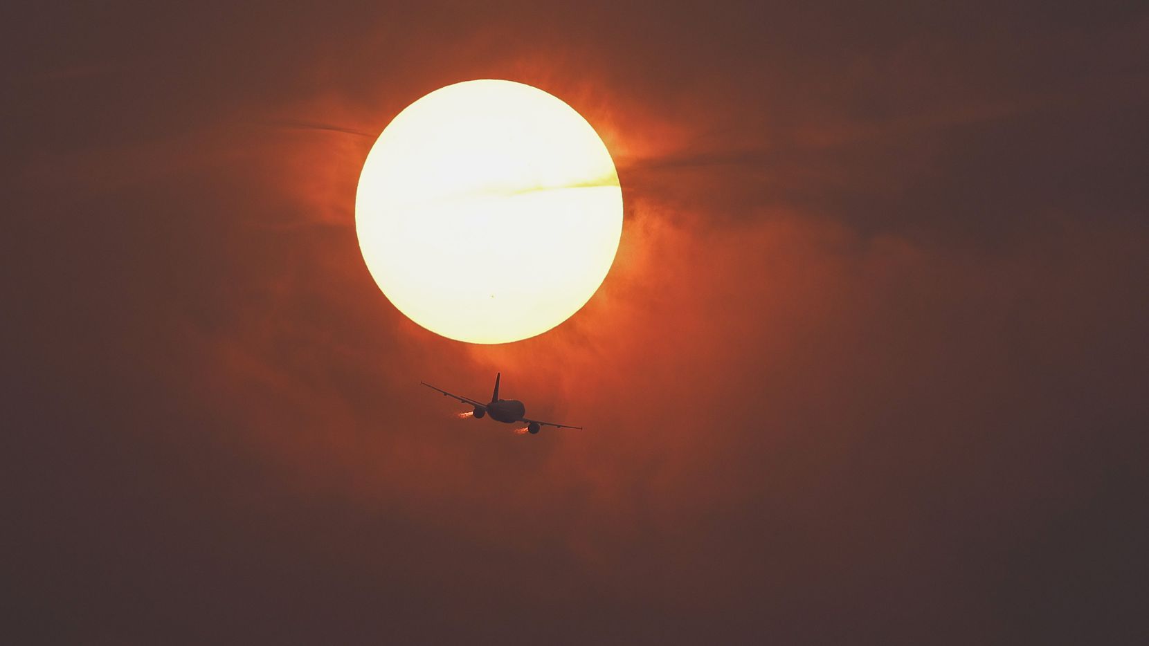 A commercial airline flies past the sun covered in haze made from smoke of Canadian...