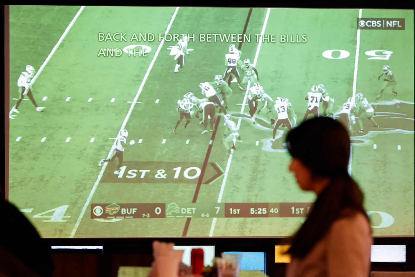 Attendees walk around by a TV screen broadcasting football during the fifth annual...