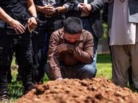 Altaf Hussain cries over the grave of his brother Aftab Hussein at Fairview Memorial Park in...