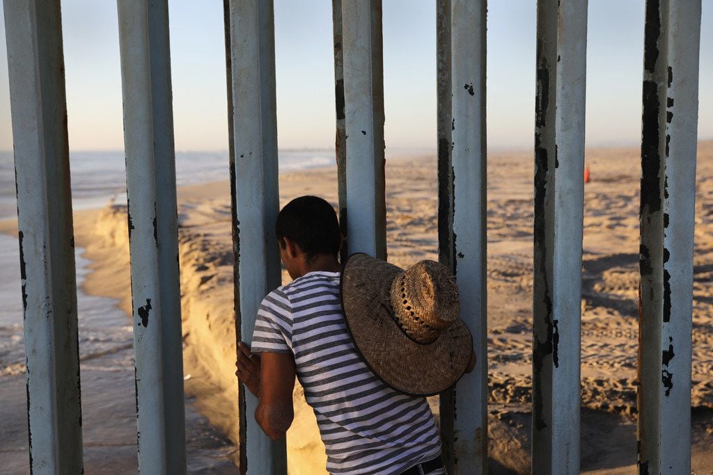   A man looks through the U.S.-Mexico border fence into the United States on September 25,...
