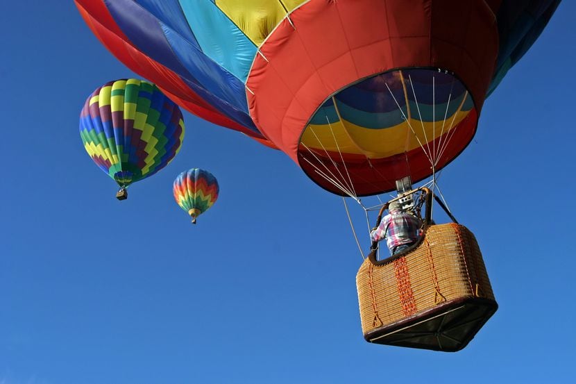 A brightly colored hot air balloon ascends into a cloudless blue sky, where two other...