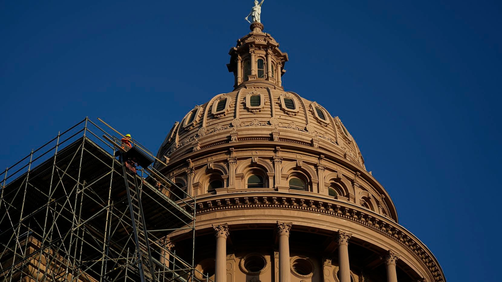Construction workers move material for a roof restoration project at the Texas Capitol as...