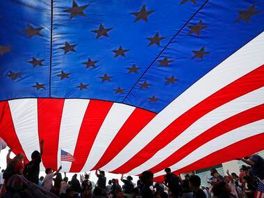 Youngsters sit under a large flag for side on the Dallas City Hall Plaza after the Mega...