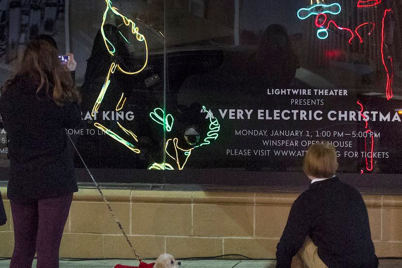 Passersby stop to watch and photograph the Lightwire Theater performance in the windows of...