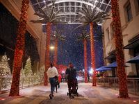 Visitantes de Galleria Dallas caminan bajo la nieve artificial que cae cada día en la...