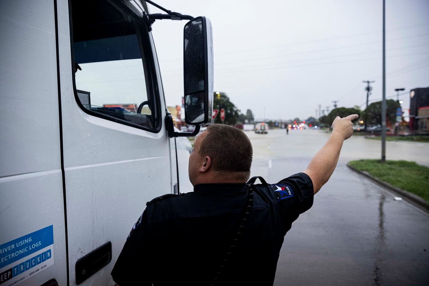 An officer directs a semi truck diver around the flooded road at Military Parkway and...