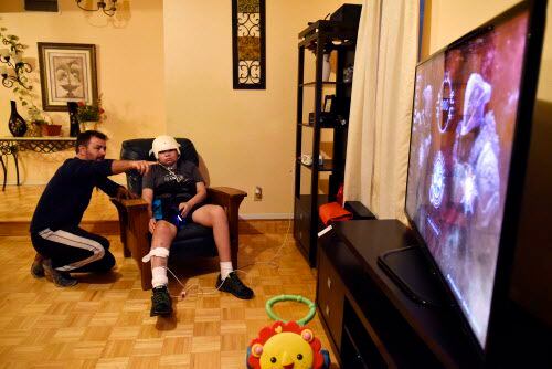 Andrés Gómez ayuda a su hijastro Esteban Monreal, 16, a jugar un videojuego en su casa en...