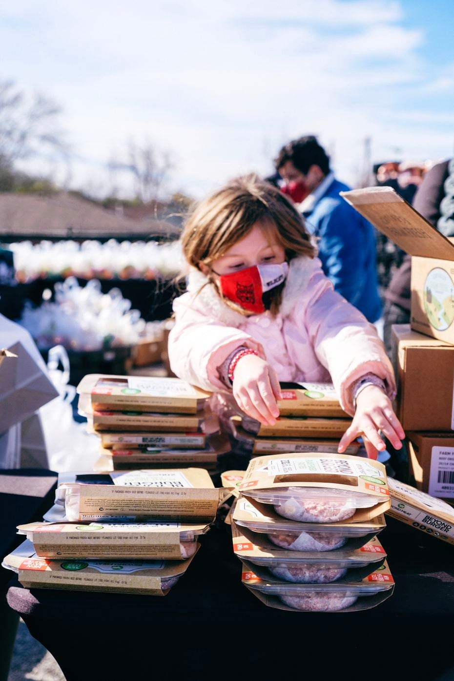 A child wearing a mask and pink coat reaches for a box of food as part of Goodr's pop-up...