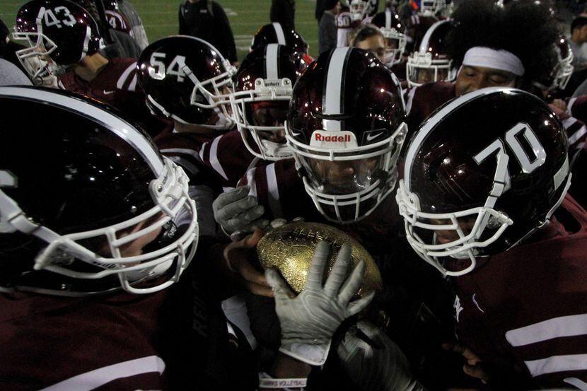 Members of the Red Oak Hawks marvel at the golden football atop a trophy presented after...