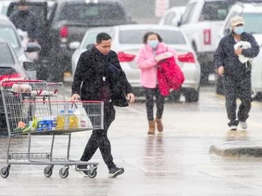 Shoppers at a Costco store in Plano navigate a cold rain as they head to their cars on...
