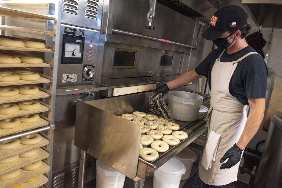 Justin Shugrue, bagel baker and founder of Shug's Bagels, seasons both sides of a batch of...