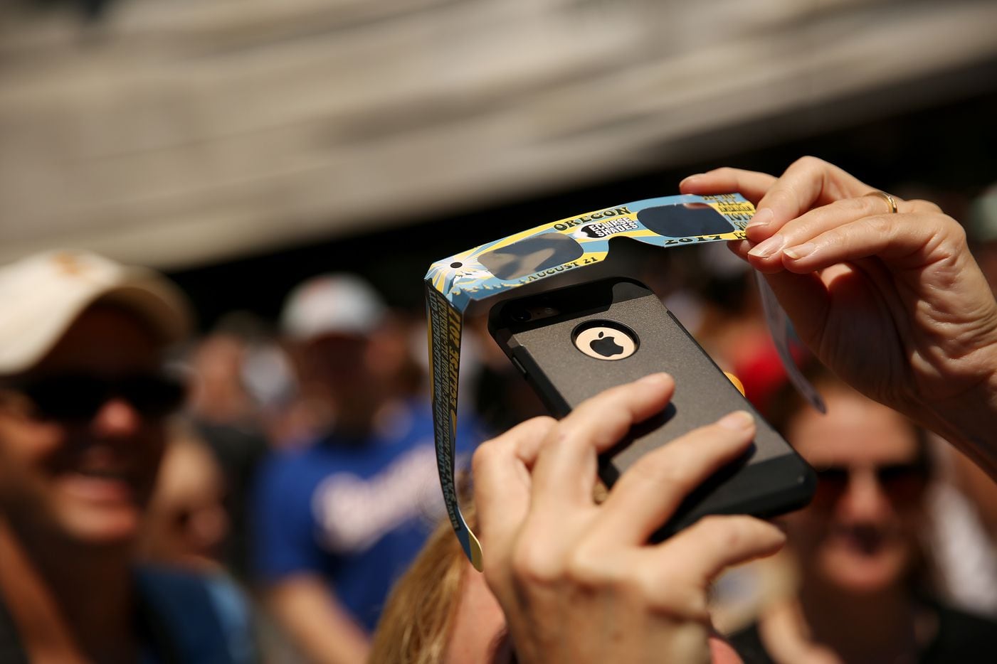 A person attempts to take a photograph of the sun through  pair of glasses during a solar eclipse outdoor watch party at the Perot Museum of Nature and Science.