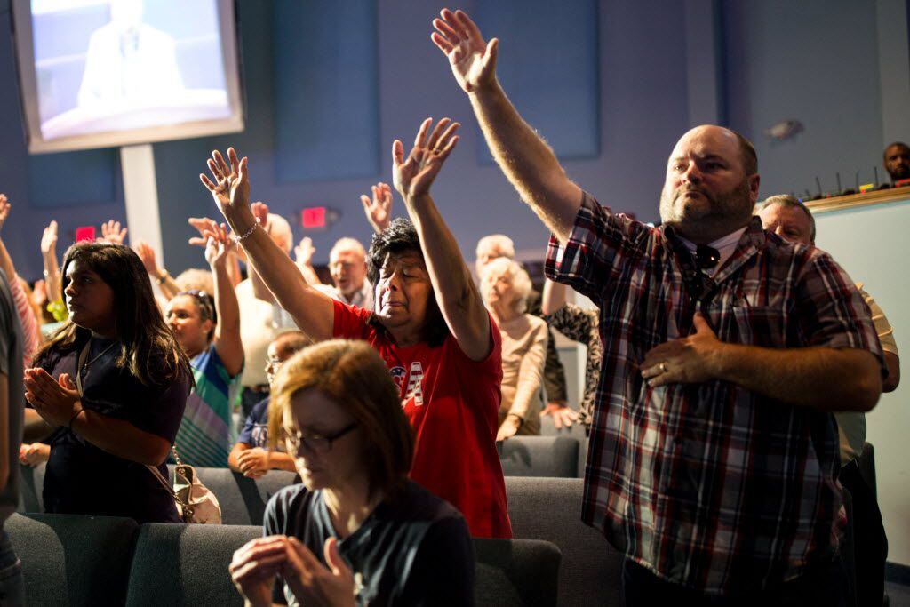 Helen Davis (center), and Craig Davis (right) prays with their hands raised during the...