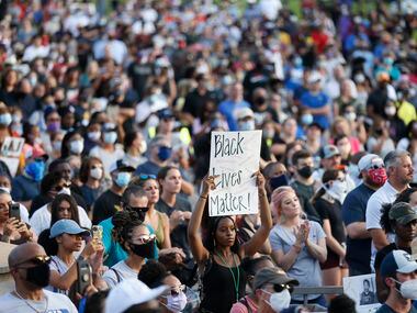 A woman holds up a sign as people stand together during a prayer vigil as various pastors...