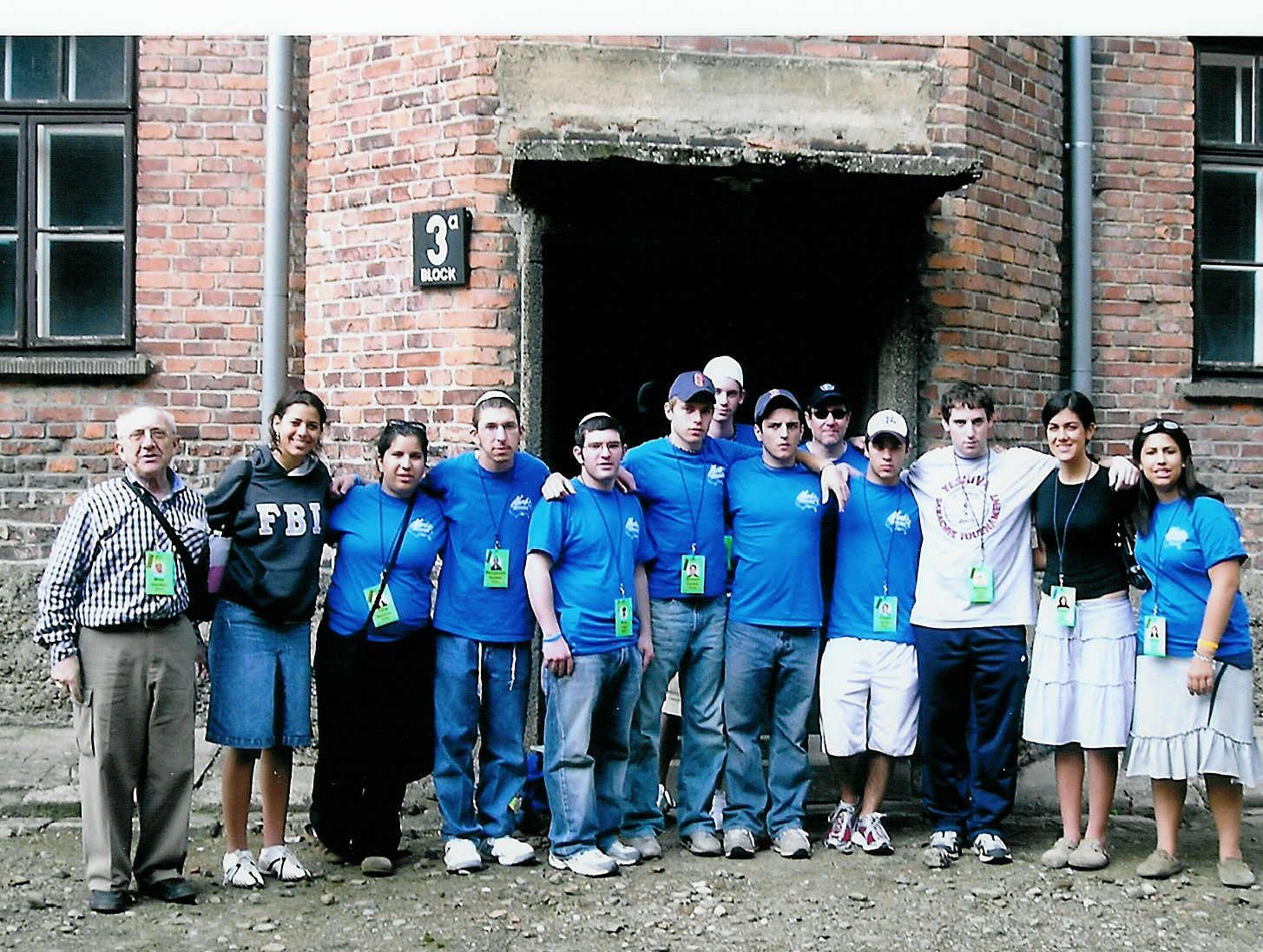 An undated photo taken in roughly 2005; Yavneh Academy's March of the Living participants, (from left to right) Rachelle Krasoff, Tina Newman, Benjamin Epstein, Ben Fine, Simon Chafetz, Shane Lazarus, Jeremy Issakarian, Mike Zucker, Chad Davis, Benny Fried, Eliza Lavi and Abby Coben, with Max Glauben, (far left) at Auschwitz. 
